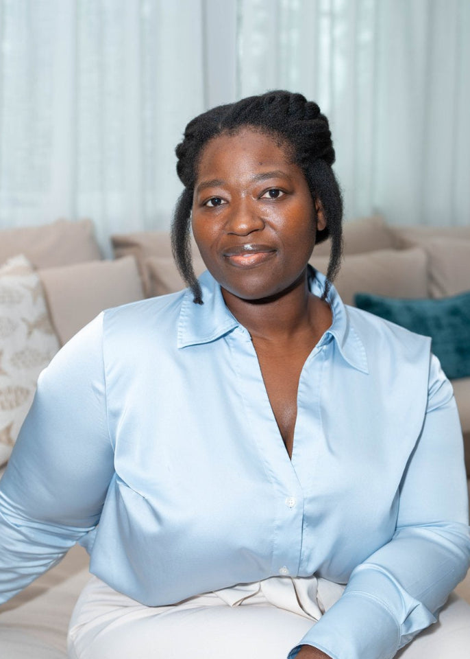 Woman sitting on a couch wearing a light blue shirt and white pants.