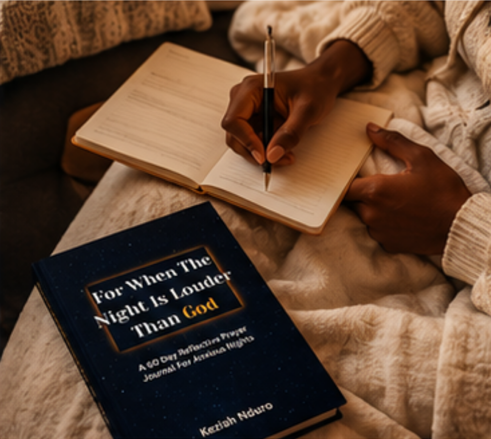 A cozy lifestyle scene showing a person writing in an open notebook with a pen, with a dark blue reflective journal titled 'For When The Night Is Louder Than God' by Keziah Nduro lying nearby on a soft blanket.